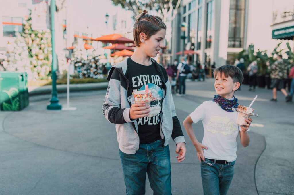 Two boys walking together in a city area enjoying ice cream on a sunny day.